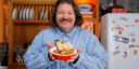 Matty Matheson holding an egg bake recipe topped with tomato sauce, potatoes, and sausage, served with cheesy bread.